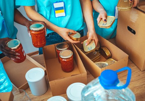 Charity workers placing food into donation boxes for a community outreach food drive of support and help people in Ukraine. Group of volunteers preparing food donations for people in need in Ukraine