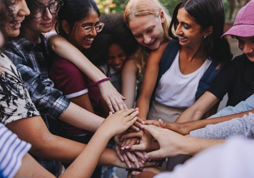 Diverse teenagers smiling cheerfully while putting their hands together in a huddle. Group of generation z youngsters symbolizing team spirit and togetherness.